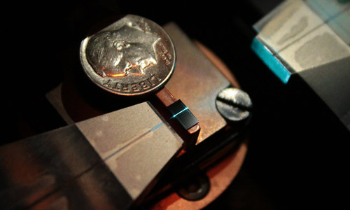 This small rectangular chip has been fabricated with numerous circuits designed to change the wavelength of laser light. In the photo, one of these circuits is shown converting invisible infrared light into visible blue light. (A dime provides a size comparison.) Credit:&nbsp;R. Jacobson/NIST.&nbsp;
