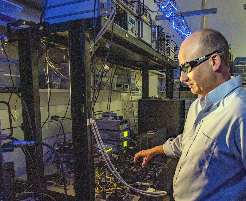 One, two... NIST physicist Thomas Gerrits adjusts the laser beam hitting a detector. The squiggly overhead light helps researchers see the lab setup without disturbing the detectors, which are insensitive to blue light. Credit: J. Burrus/NIST.