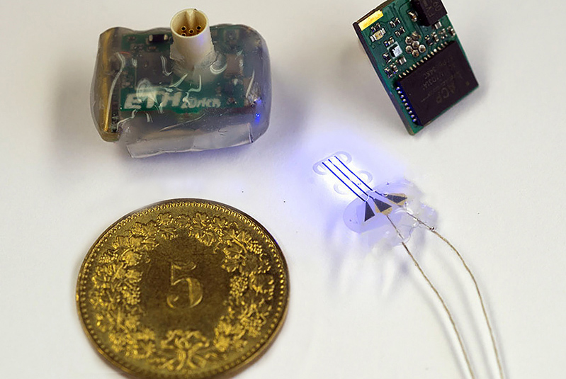 The small LED control unit (top left) and the LED implants (bottom right) form the new neurotechnology platform. Top right: assembled circuit before mounting the battery and packaging in silicone. Swiss 5 cent piece for scale, which has a diameter of 17.15 mm.