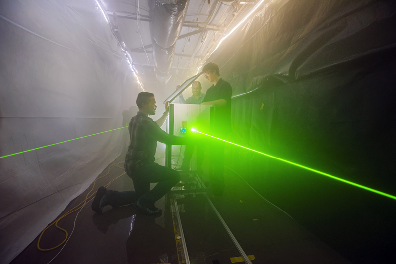 Andres Sanchez, left, Jeremy Wright, center, and Brian Bentz prepare for an optical test in Sandia National Laboratories' fog facility. Bentz is leading a three-year project to use computational imaging to detect, locate and image objects in fog. This photo was taken prior to the COVID-19 pandemic. (Photo by Randy Montoya) Click on the thumbnail for a high-resolution image