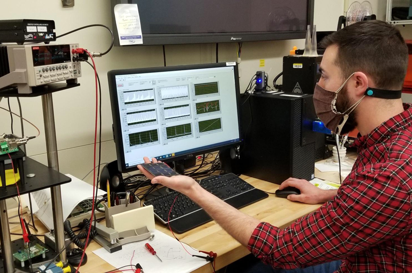 NIST researcher Andrew Shore holds a miniature high efficiency solar device as it charges a sensor using indoor light as an energy source. Credit: NIST.