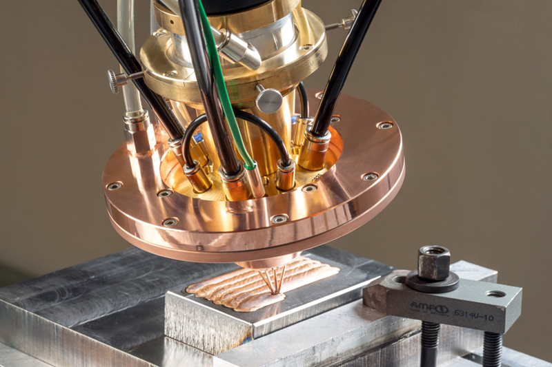 For the first time, simultaneous processing of powder and wire in various combinations becomes possible thanks to COAXquattro. The materials meet in the laser focus above the component surface, where the laser melts the coating metal. Directly on the surface, the coating is created in-situ from the powder and the individually fed wires. &copy; ronaldbonss.com/Fraunhofer IWS