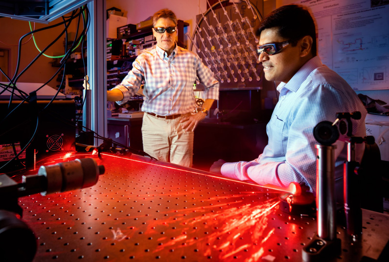 As a red beam of light is reflected in an arch, Prasad Iyer, right, and Igal Brener demonstrate optical hardware used for beam steering experiments at Sandia National Laboratories' Center for Integrated Nanotechnologies. Photo: Craig Fritz, SNL.