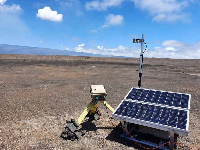 The sulfur dioxide (SO<sustrong>2</sustrong>) gas camera installation on K&imacr;lauea volcano, Hawaii. A faint gas plume can be seen rising from the crater at the centre of the image and drifting to the left. The flank of Moana Loa is in the background. Photo: Tom Pering.