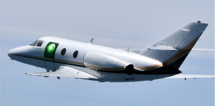 A test aircraft carries the sub-scale HARDROC beam director illuminated by a low-power scoring laser during an experimentation flight in 2022. The HARDROC program evaluated in flight the ability of various aerodynamic flow control techniques to mitigate optical and mechanical distortions imparted on a laser beam leaving an airborne platform travelling at high speeds. Photo: USAF AFRL.
