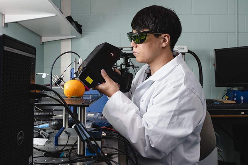 Purdue postdoctoral fellow Sungho Shin uses a portable LIBS spectroscopy instrument to collect data from the surface of an orange. Credit:Purdue University/Charles Jischke.