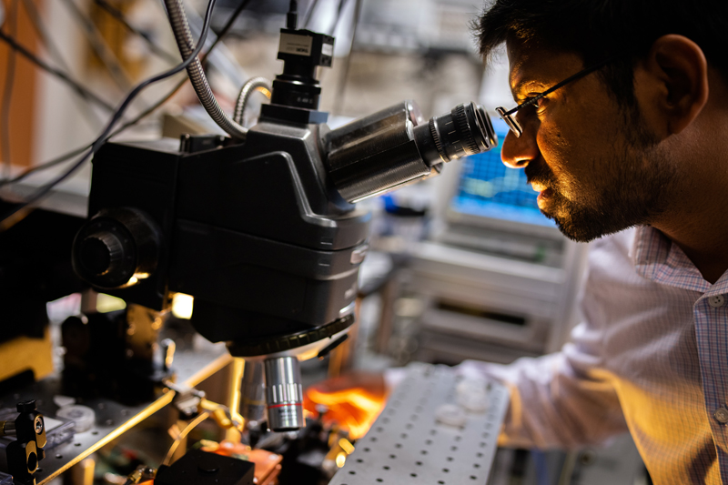 Sandia National Laboratories scientist Ashok Kodigala aligns a fiber to a chip-scale, heterogeneously integrated laser under a microscope at the MESA complex.  Photo credit: Craig Fritz.