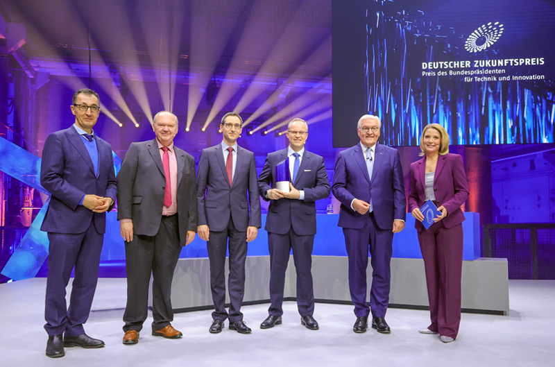 Winners of the Deutscher Zukunftspreis 2024, Dr. Norwin von Mal (center), Stefan Gr&ouml;tsch (third from right) and Dr. Hermann Oppermann (second from left) with Federal President Frank-Walter Steinmeier (second from right), Federal Minister for Education and Research Cem Ã–zdemir (left) and moderator Yve Fehring (right).