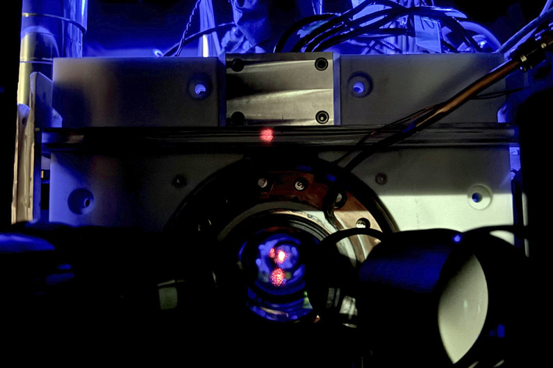 An extremely cold gas of strontium atoms is trapped in a web of light known as an optical lattice. The atoms are held in an ultrahigh-vacuum environment, which means there is almost no air or other gases present. This vacuum helps preserve the atoms' delicate quantum states, which are fragile. The red dot you see in the image is a reflection of the laser light used to create the atom trap. Credit: K. Palubicki / NIST.