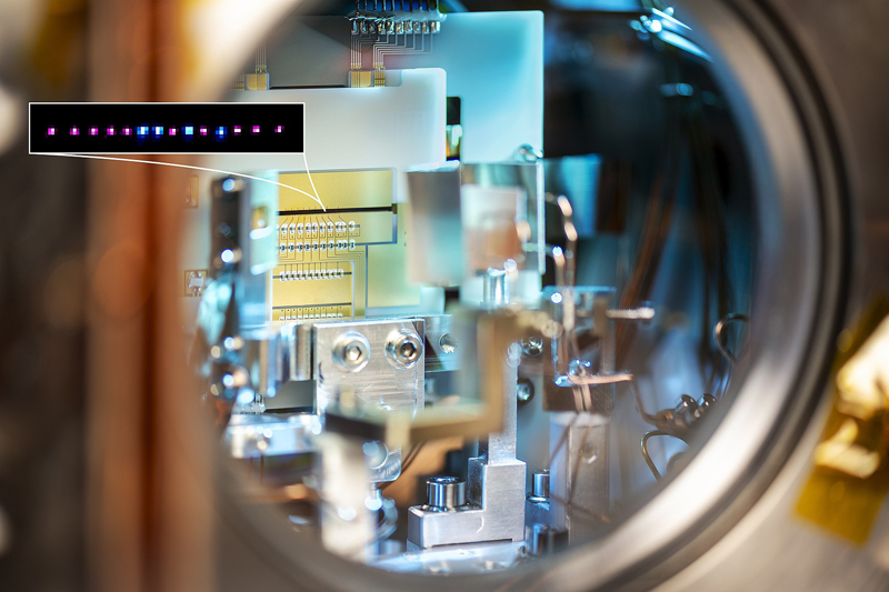 The ion trap of the new In+/Yb+ crystal clock in its vacuum chamber. The ions are trapped in the gap that can be seen in the middle of the image between the gold electrodes (arrow). Inset image: a crystal made of indium (pink) and ytterbium ions (blue).