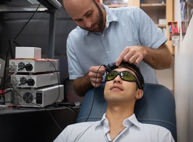 Caltech postdoctoral scholar Simon Mahler is shown here placing the SCOS device on the head of graduate student Yu Xi Huang. The new device is affordable and compact, making it ideal for stroke assessment in a clinical setting. Credit: Caltech.