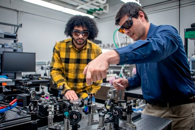 Bilal Hassan (left), a PhD student in aerospace engineering, discusses how to configure a pulse shaper with Christopher Limbach (right). With funding from the Air Force Office of Scientific Research, Limbach is leading a team that aims to enable satellites to share energy and momentum through laser interlinks. Credit: Jason Bolton, Aerospace Engineering, University of Michigan.