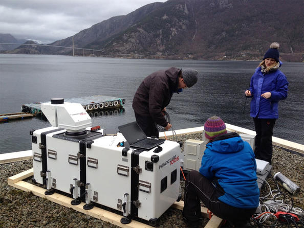 Researchers prepare a long-range lidar laser instrument WindCube100S, which is deployed at the Lysefjord center. The Lysefjord bridge is in the background. Jasna B. Jakobsen (from behind) and Etienne Cheynet, both from UiS, and Valerie Kummer from UiB. (Photo: Benny Svardal / CMR)